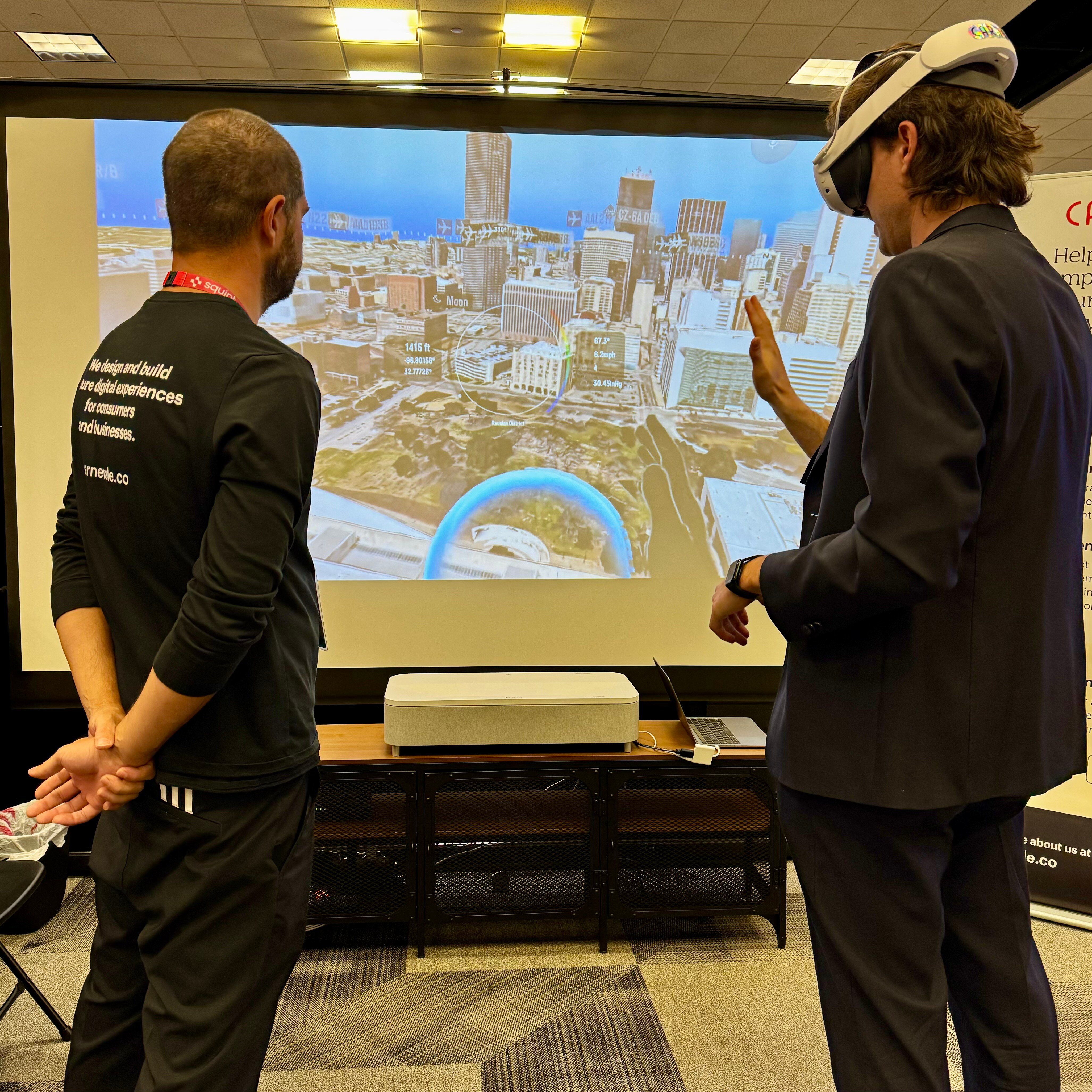 At the Augmented Enterprise Summit (AES) in Dallas, Lee, CARNEVALE's Lead AR/VR Developer, observes a person wearing a VR headset, demoing CARNEVALE's SkyLens, a dynamic data lens. This individual is interacting with a virtual city skyline with hand motions and voice control.